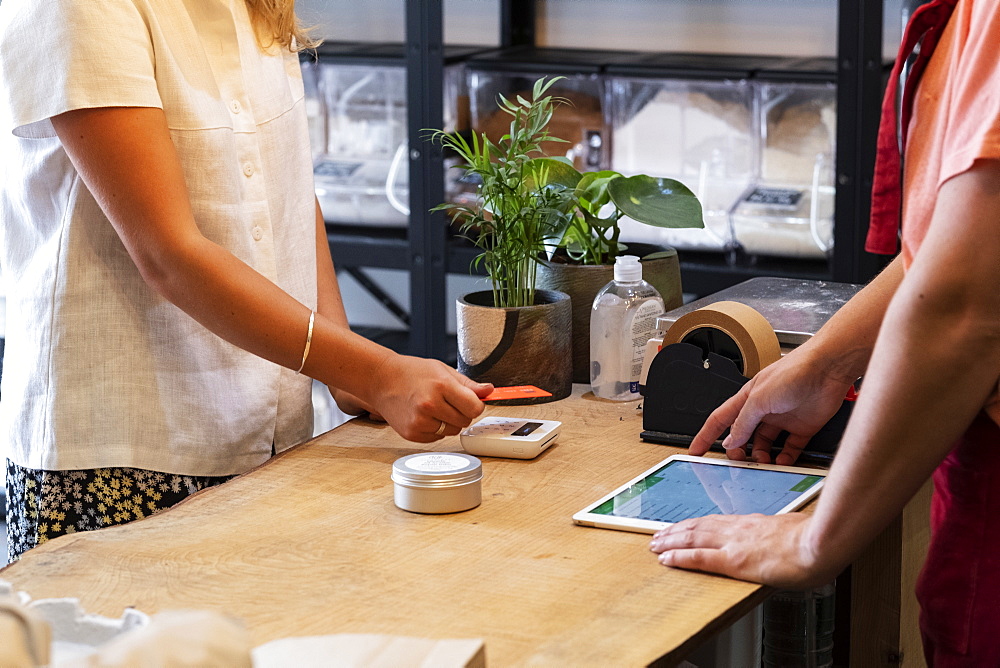 Woman shopping in waste free wholefood store, making contactless payment with her credit card, Watlington, Oxfordshire, United Kingdom