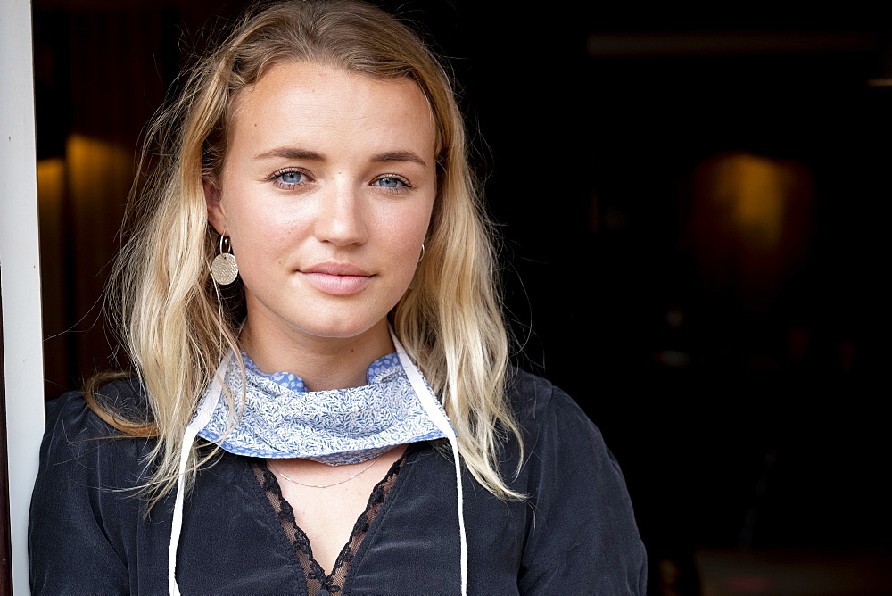 Portrait of young blond woman wearing face mask around her neck, smiling at camera, Watlington, Oxfordshire, United Kingdom