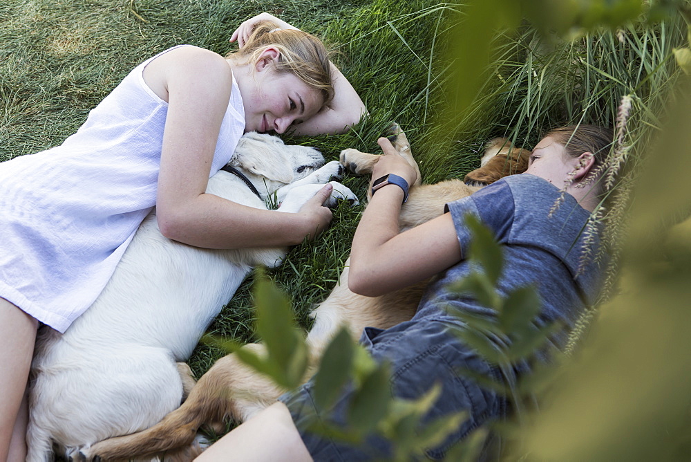 Two teenage girls lying on lawn, hugging their Golden Retriever dogs, New Mexico, United States