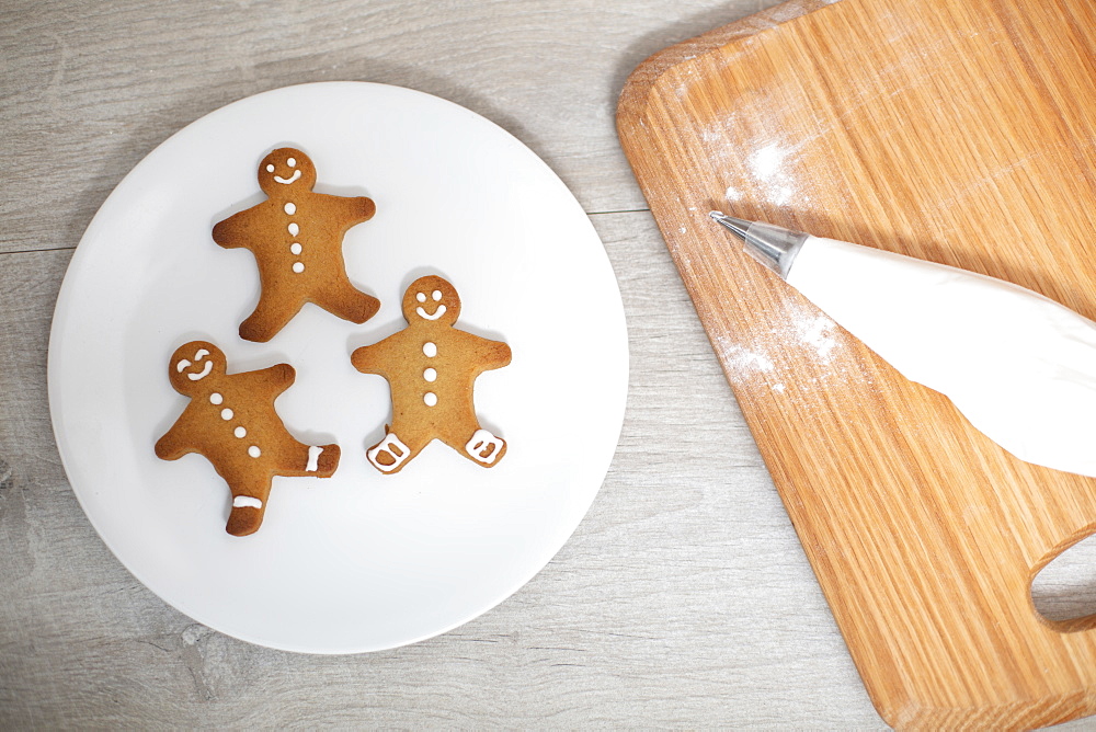 High angle close up of wooden cutting board and Gingerbread Men on a white plate