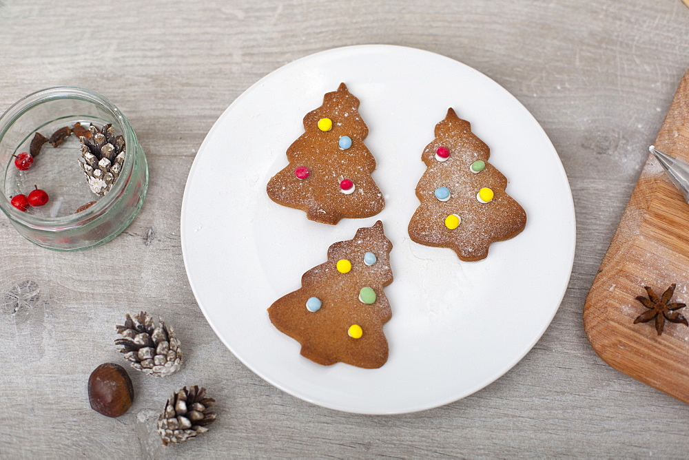 High angle close up of Christmas decorations and Christmas Tree cookies on a white plate