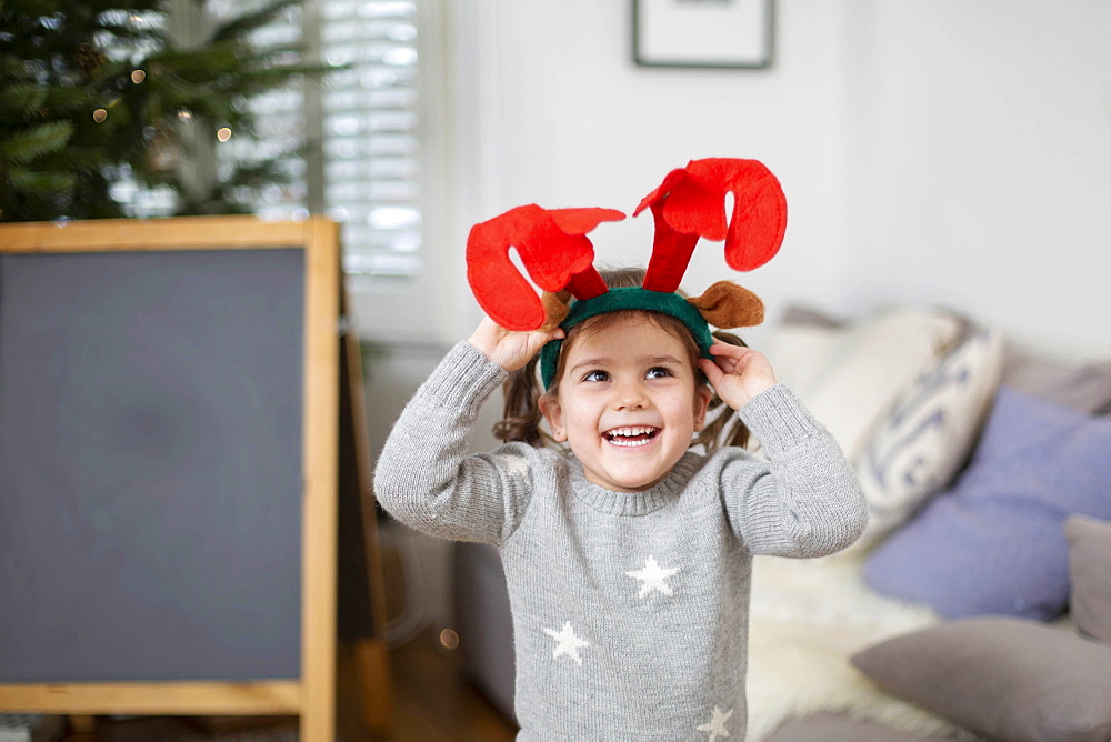 Smiling young girl wearing grey jumper putting on reindeer antler headband