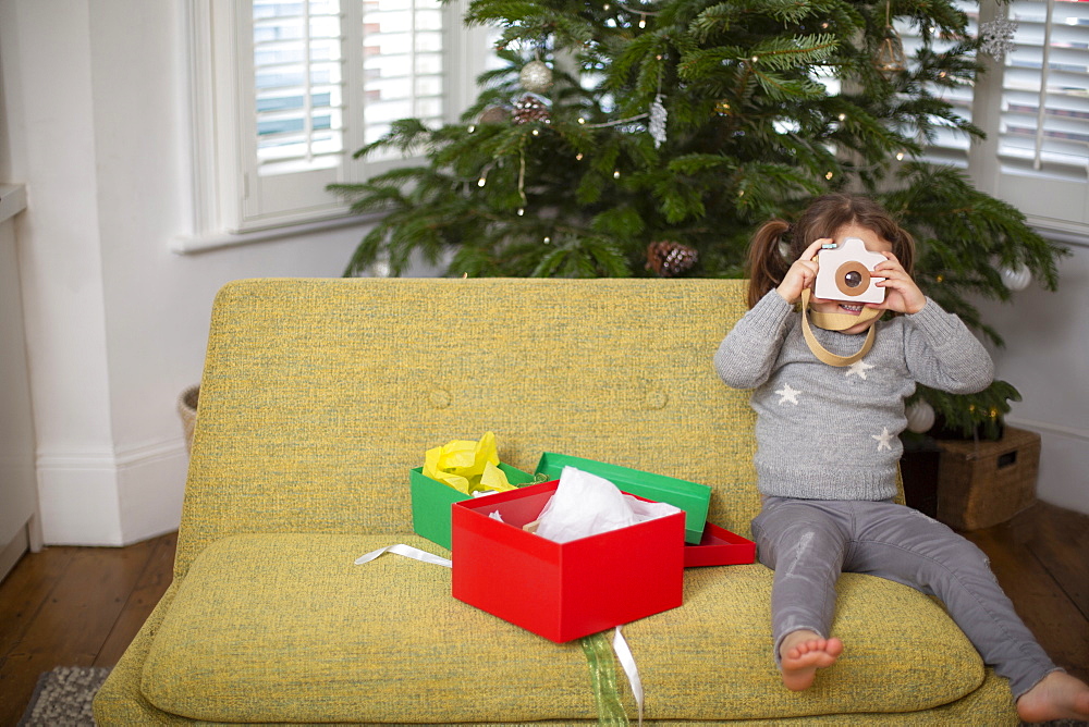 Young girl sitting on sofa with Christmas present taking picture with toy camera