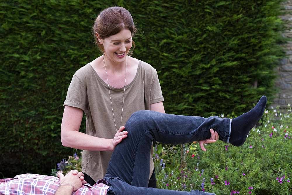 Man on a couch and therapist raising his leg, in a garden therapy session