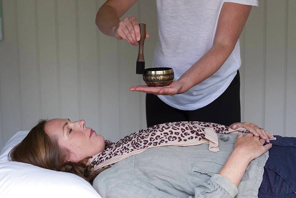 Woman on a couch, and a female therapist using Tibetan singing bowl, sound therapy