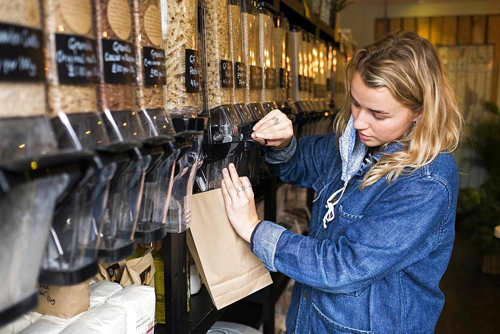 Young blond woman wearing face mask, shopping in waste free wholefood store, Oxfordshire, England, United Kingdom