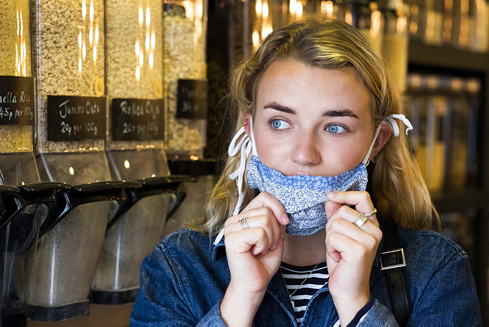 Young blond woman wearing face mask, shopping in waste free wholefood store, Oxfordshire, England, United Kingdom