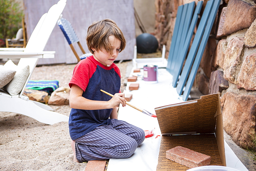 Seven year old boy using a paintbrush, painting cardboard