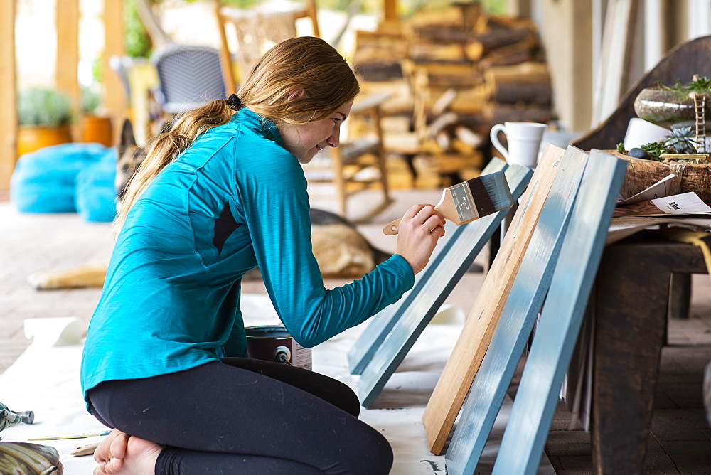 Teenage girl painting wooden shelves blue