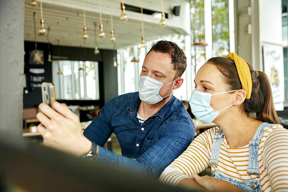 Two people wearing face masks, using a smart phone, waving during a face time call.