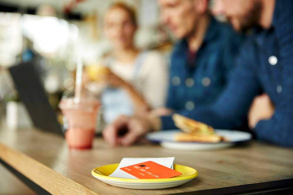 People at a cafe table, a saucer with till receipt and credit card.