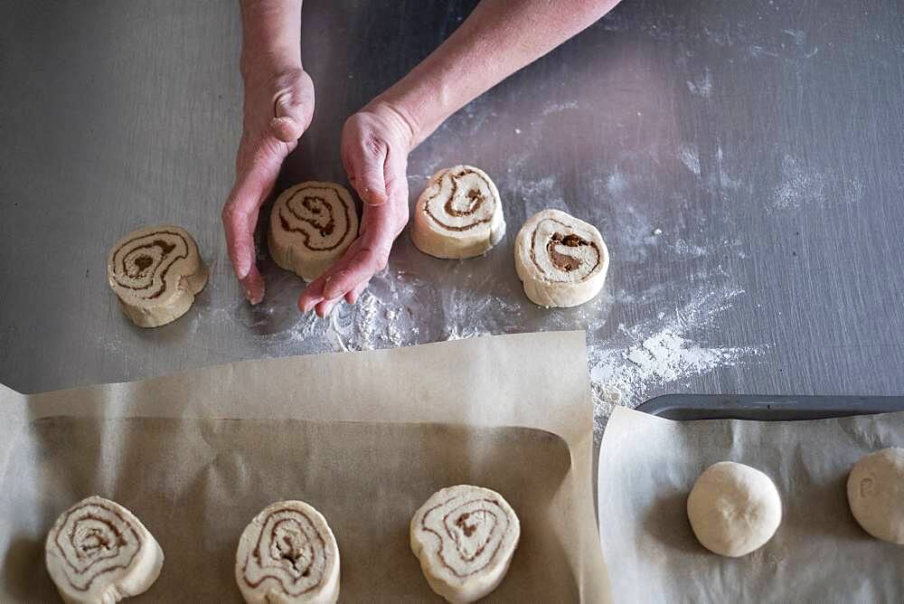 High angle close up of person shaping dough for Cinnamon Rolls on metal surface.