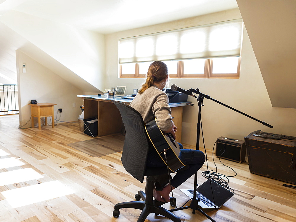 Fourteen year old teenage girl playing her guitar and singing at home in loft space