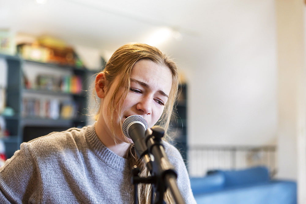 Fourteen year old teenage girl playing her guitar and singing at home in loft space