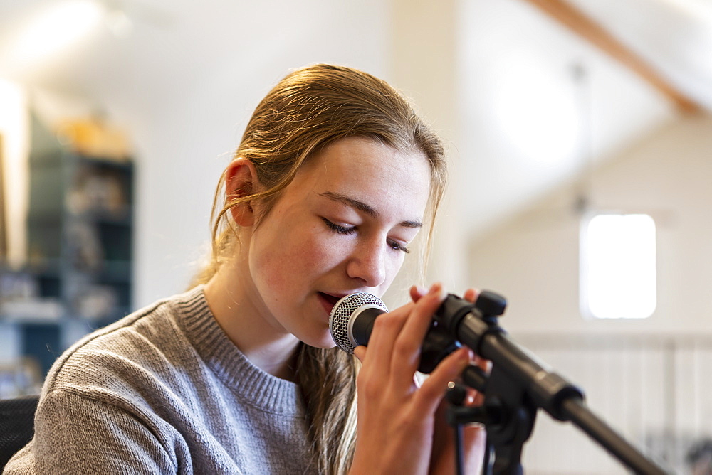 Fourteen year old teenage girl playing her guitar and singing at home in loft space