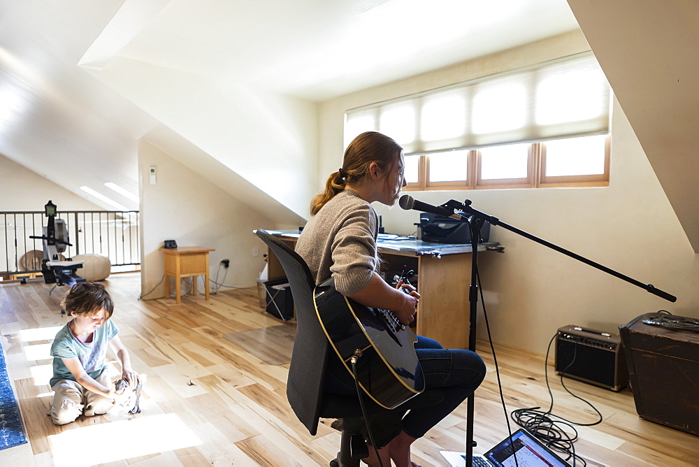 Teenage girl playing her guitar and singing, her brother playing in the background