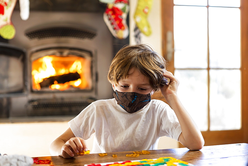 Young boy wearing mask playing board game alone at home