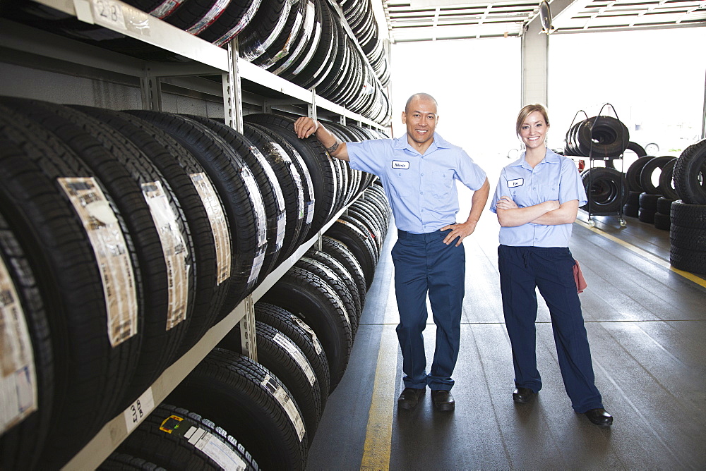 Portrait of smiling male and female mechanic by a rack of tyres in a workshop