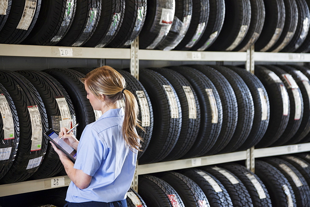 Young female mechanic takes inventory of new tires in repair shop