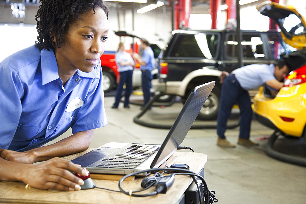 Female mechanic using a laptop, diagnostic electronics, in an auto repair shop