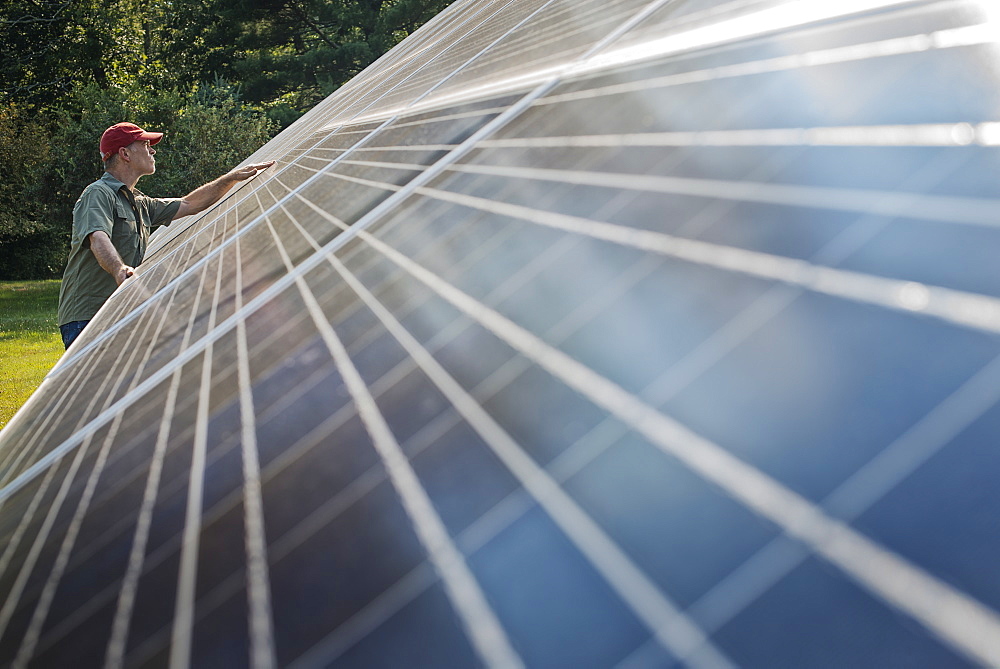 A man inspecting the surface of a large tilted solar panel installation for harnessing the energy of the sun, New York state, USA