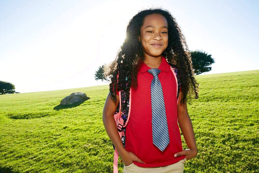 Young mixed race girl in pink shirt and formal tie, wearing a backpack