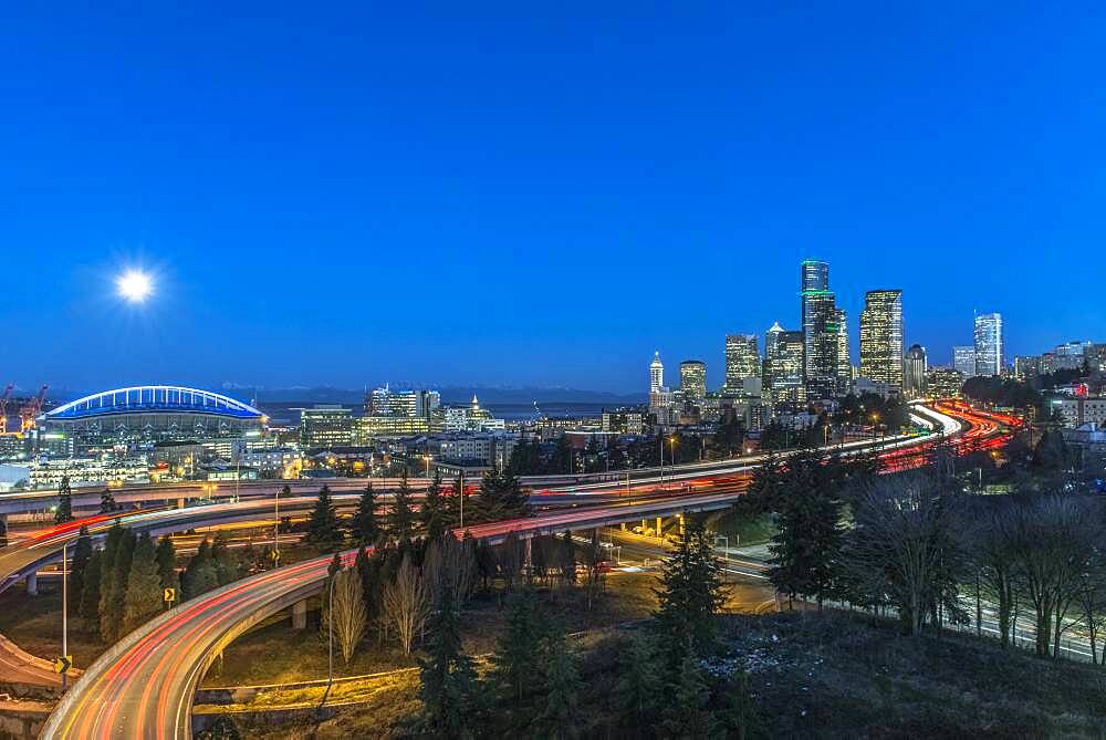 The city skyline of Seattle at night, road and bridge, downtown buildings lit up in moonlight.