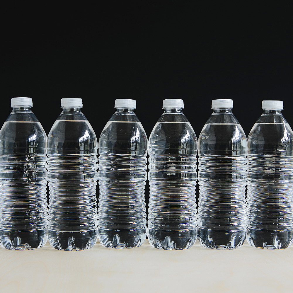 Row of clear, plastic water bottles filled with filtered water in a row, on a black background, Washington, USA