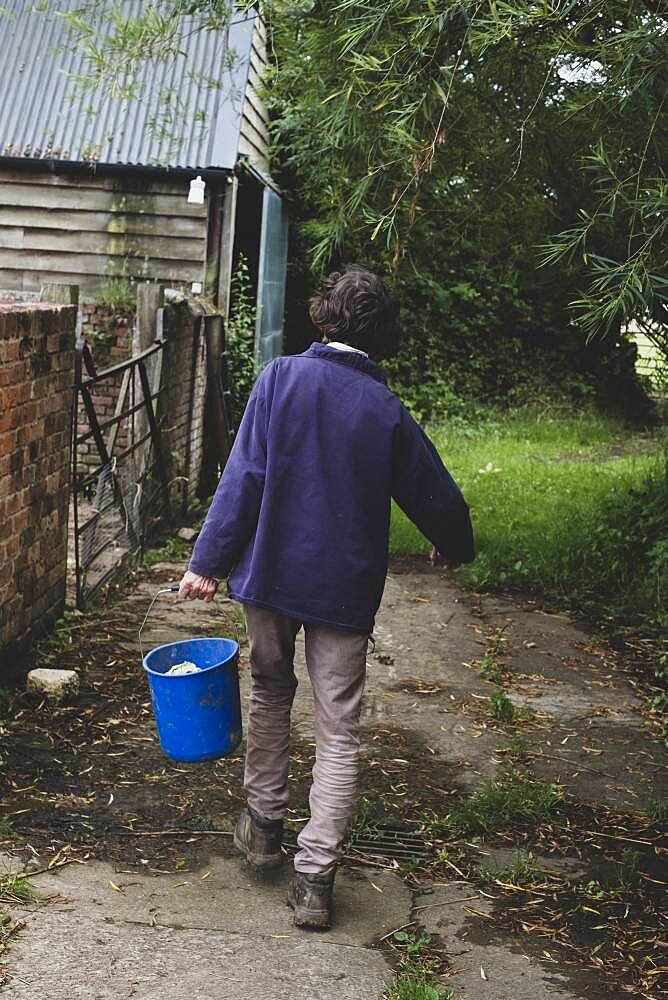 Rear view of woman on a farm, carrying blue plastic bucket.