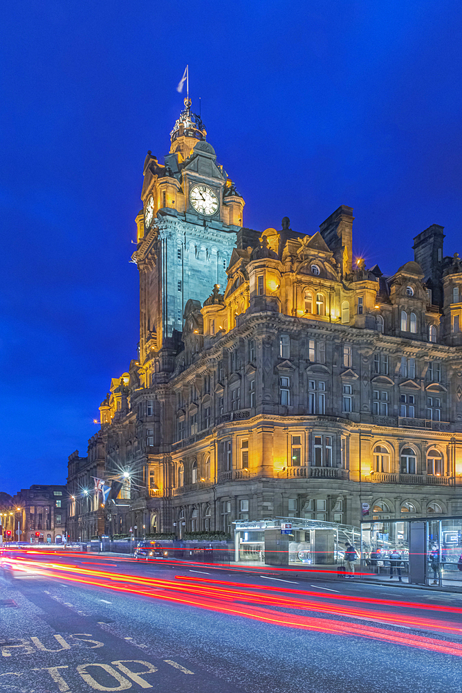 Clock tower of Balmoral Hotel lit up at night with traffic light blur below.