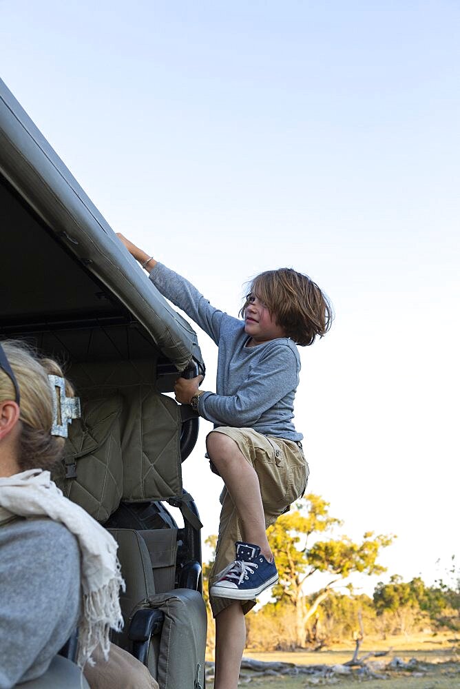 A boy climbing up the side of safari vehicle, Okavango Delta, Botswana