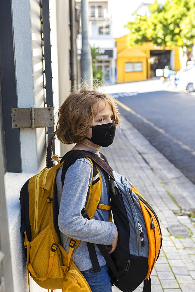 A boy carrying a backpack with a black facemask on a street, Cape Town, South Africa