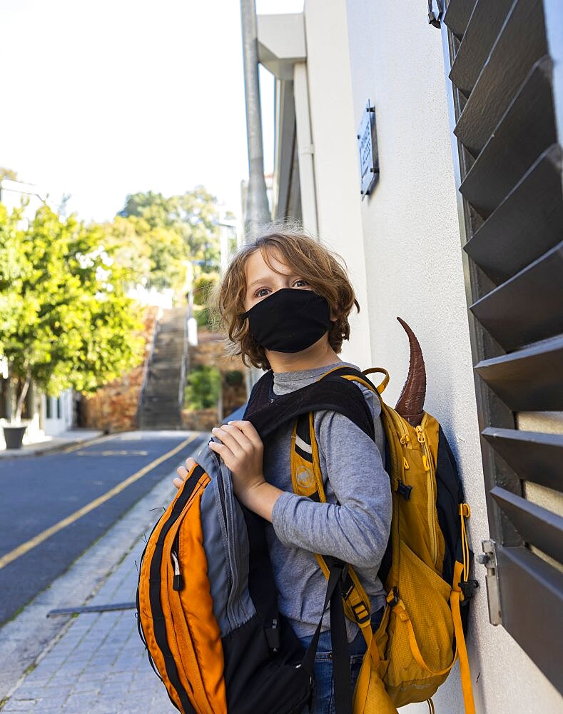 A boy carrying a backpack with a black facemask on a street, Cape Town, South Africa