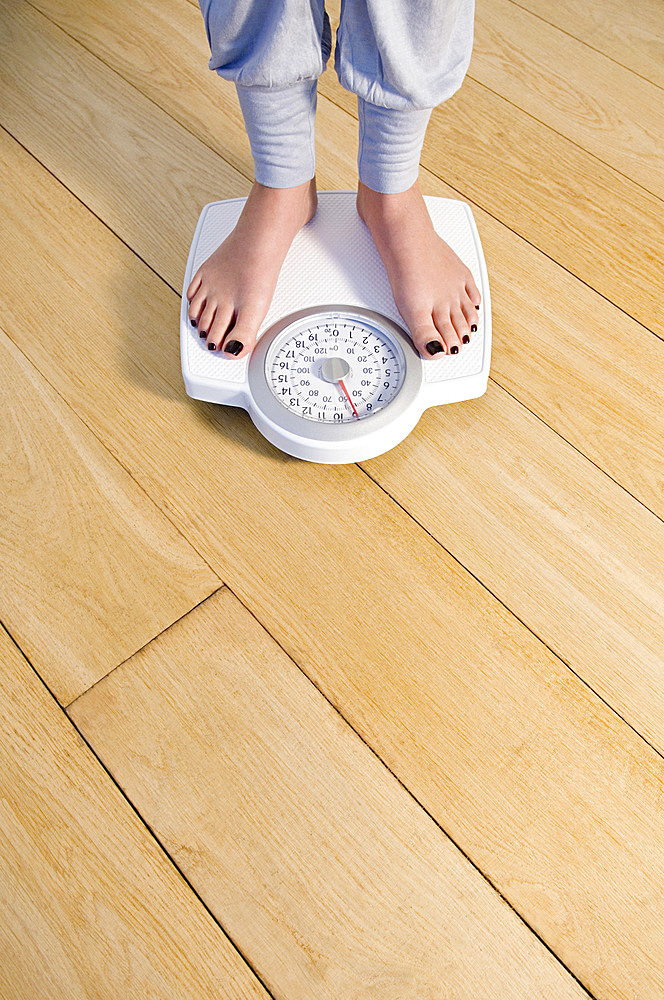 Woman standing on weighing scale, feet and lower legs.