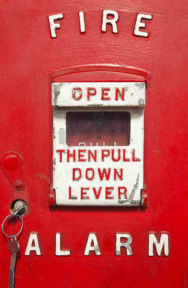 A red metal historic antique fire alarm box. An alarm lever with written instruction