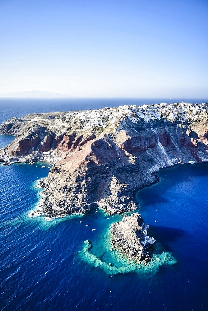 Aerial view of an island in the deep blue seas of the Aegean sea, rock formations, whitewashed houses perched on the cliffs.