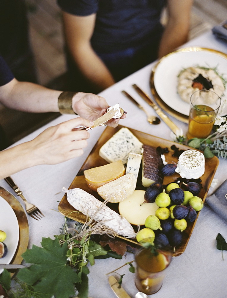 A table laid with a white cloth and place settings seen from above. An organic cheese board with soft and hard cheeses and figs. Two people sitting at the table, Provo, Utah, USA