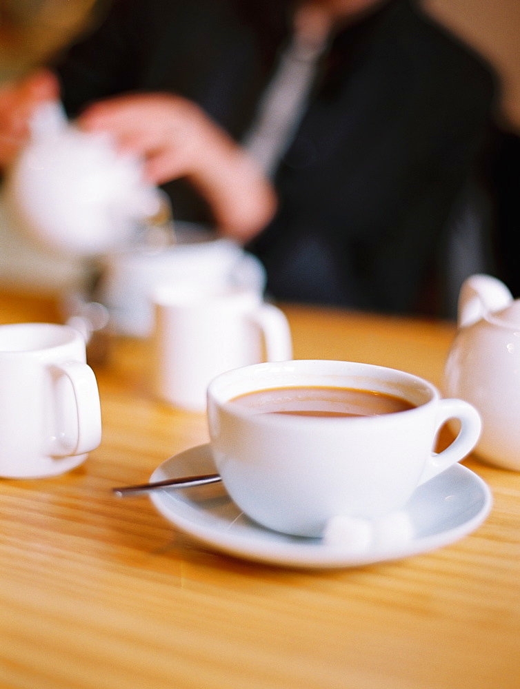 A woman seated pouring a cup of tea out of a white china tea pot, England