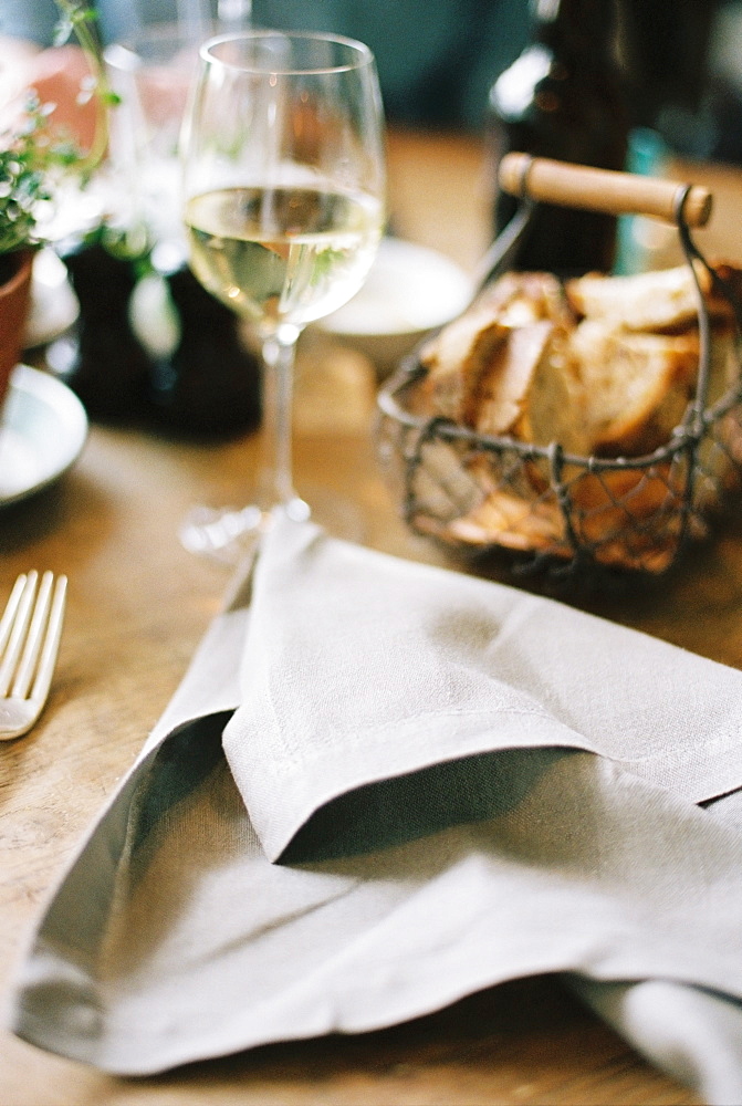 A meal laid out on a table, bread in a basket, wine in a glass and a discarded napkin, England