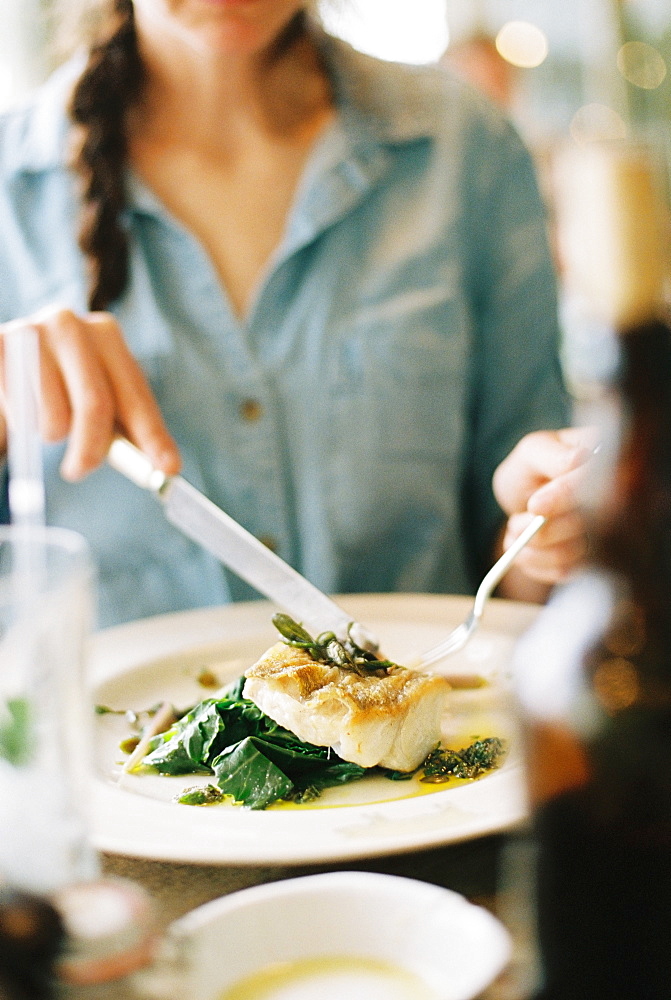 A woman eating a meal, a dish of fish and green vegetables, England