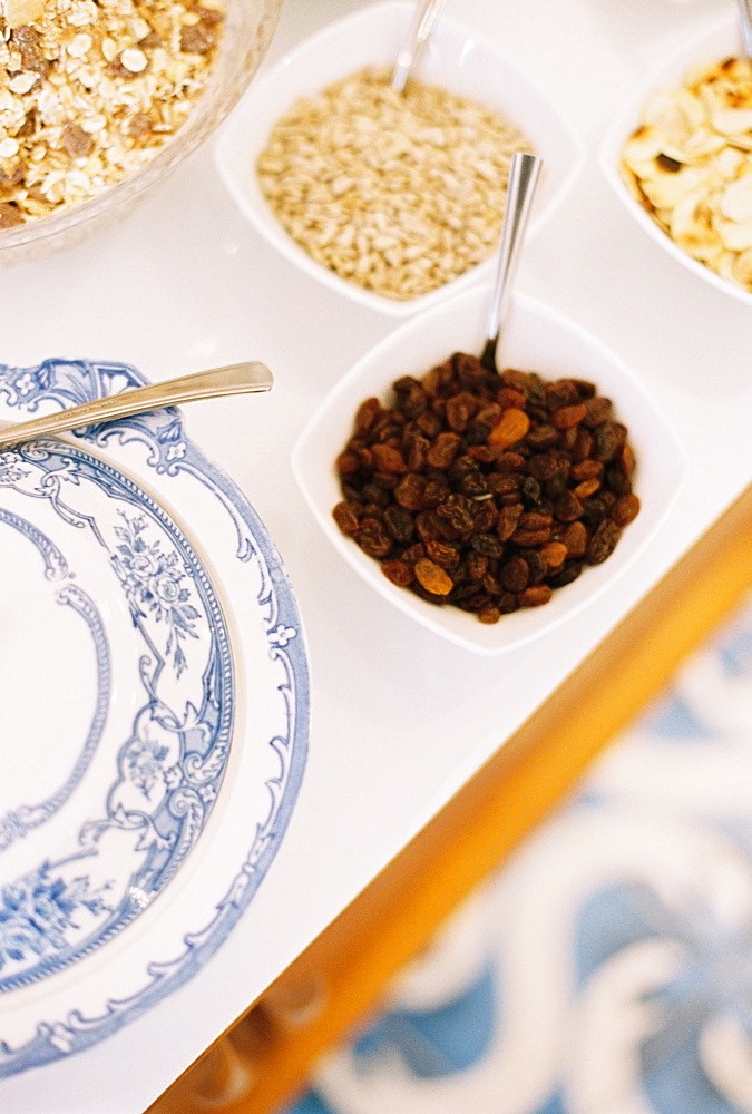 A tabletop with a blue and white plate, bowls of granola, oats and raisins, England