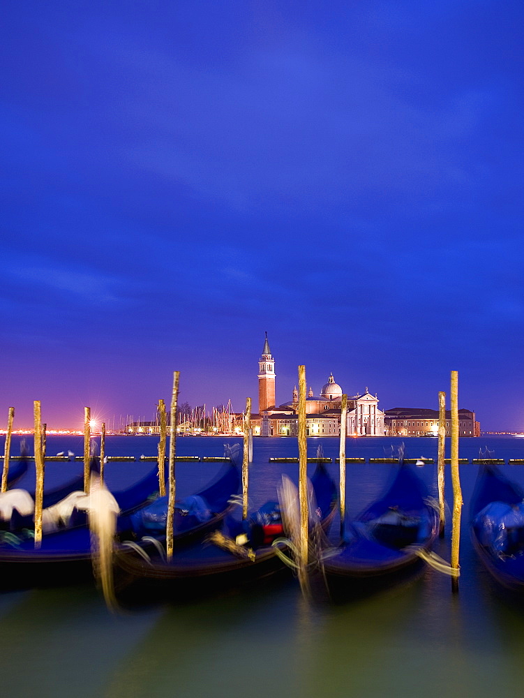 A view from the Riva degli Schiavoni and the Piazza San Marco across the water to the island and church of San Giorgio Maggiore, Gondolas moored at dusk, Venice, Italy