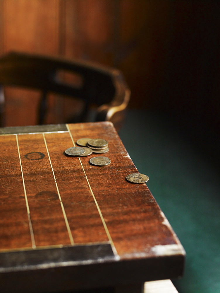 A pub games table with copper coins laid on the surface. A traditional carved chair, Pub table, England