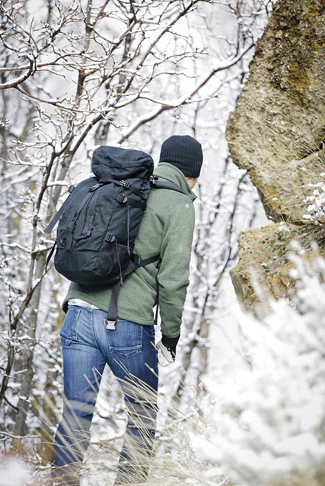 A man wearing a fleece jacket and hat, carrying a rucksack, climbing up a rocky slope, Mountains, Utah, USA