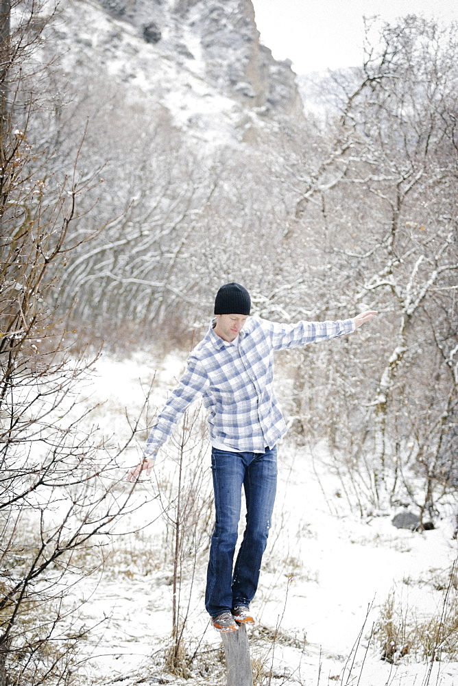 A man in the mountains in winter, balancing on a wood post in the woodland, Mountains, Utah, USA