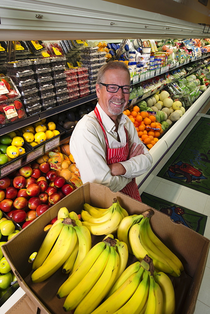 A man standing in a grocery shop beside a display of fresh fruits and vegetables.