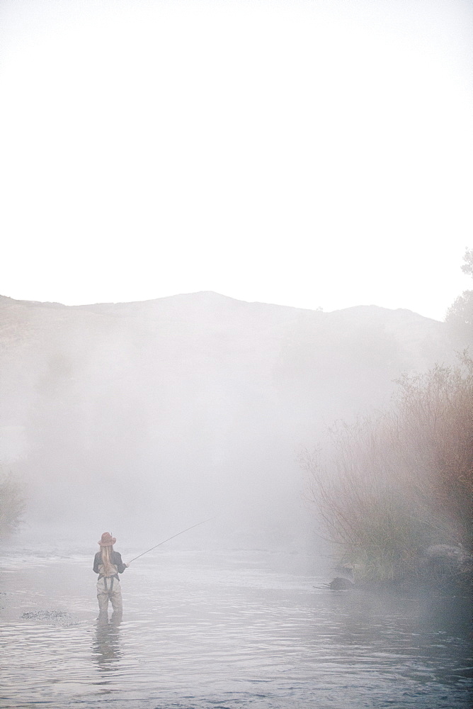 A woman fisherman flyfishing, standing in waders in thigh deep water.