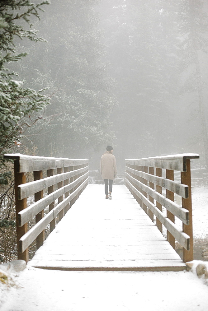 A woman walking on a footbridge in the mountains in snow.