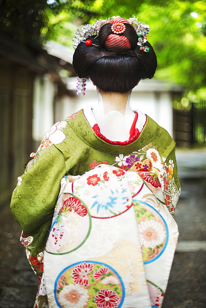 A woman dressed in the traditional geisha style, wearing a kimono and obi, with an elaborate hairstyle and floral hair clips, with white face makeup with bright red lips and dark eyes on a street, Japan