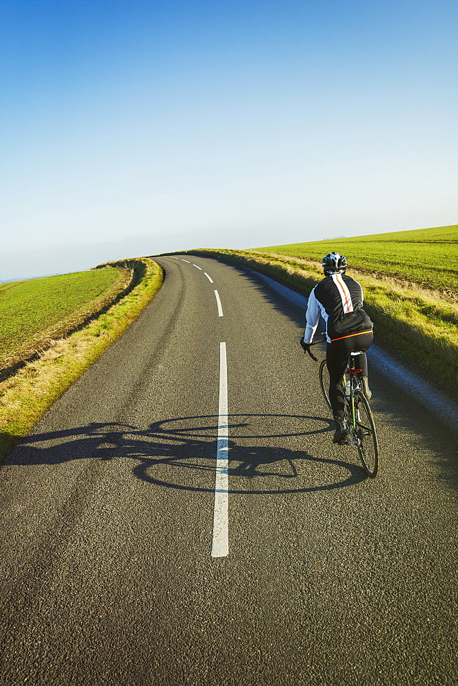 A cyclist pedalling along a country road, rear view.